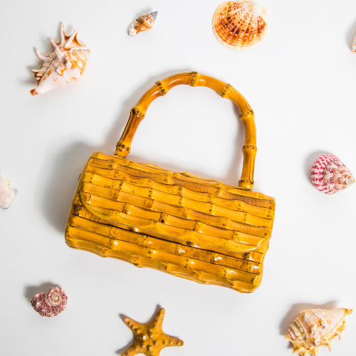 Yellow bamboo-style clutch with curved handles, styled with beach shells for a tropical summer vibe.